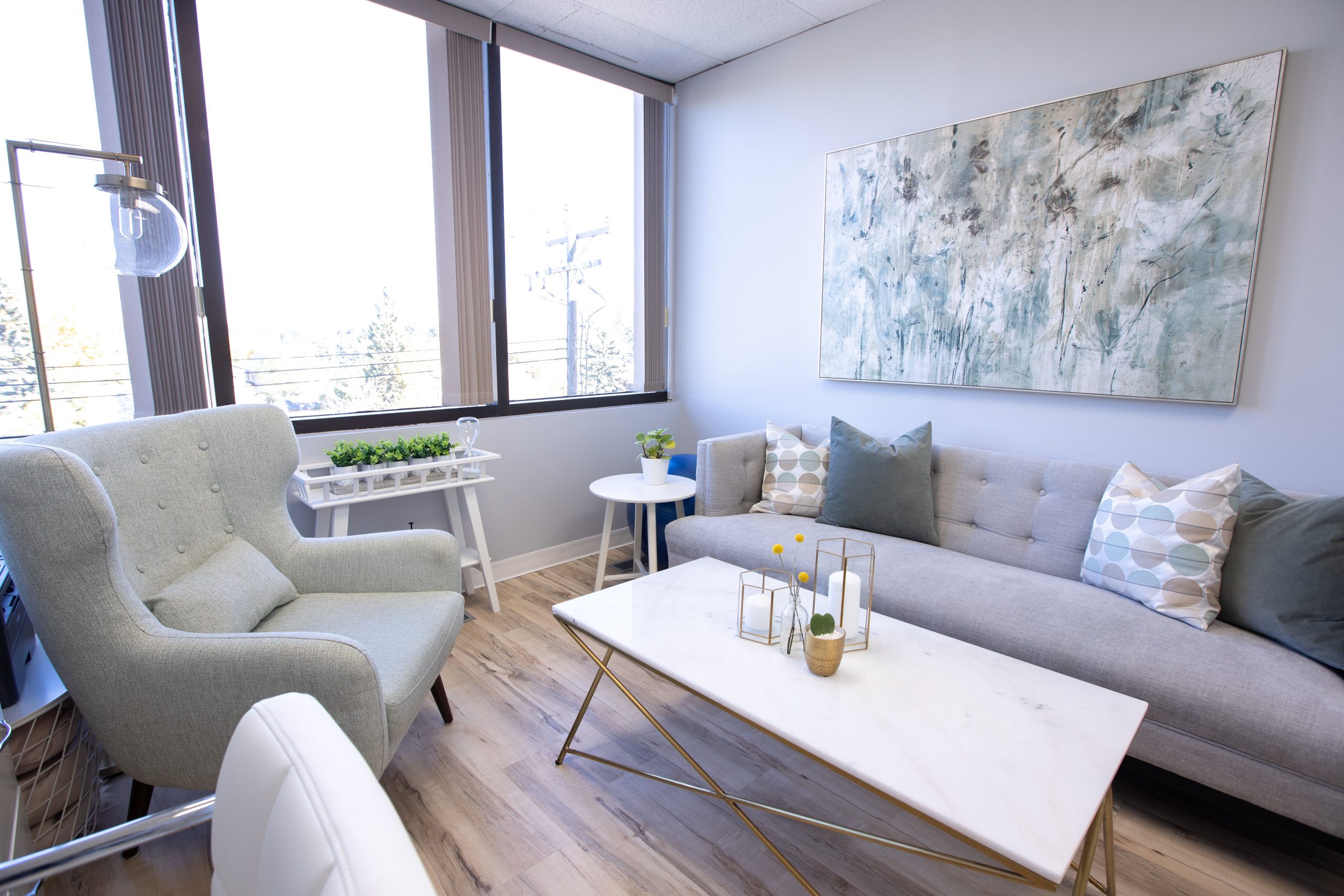 Welcoming office interior. An armchair to the left, a sofa to the right. Soft sunlight through a window in the background.