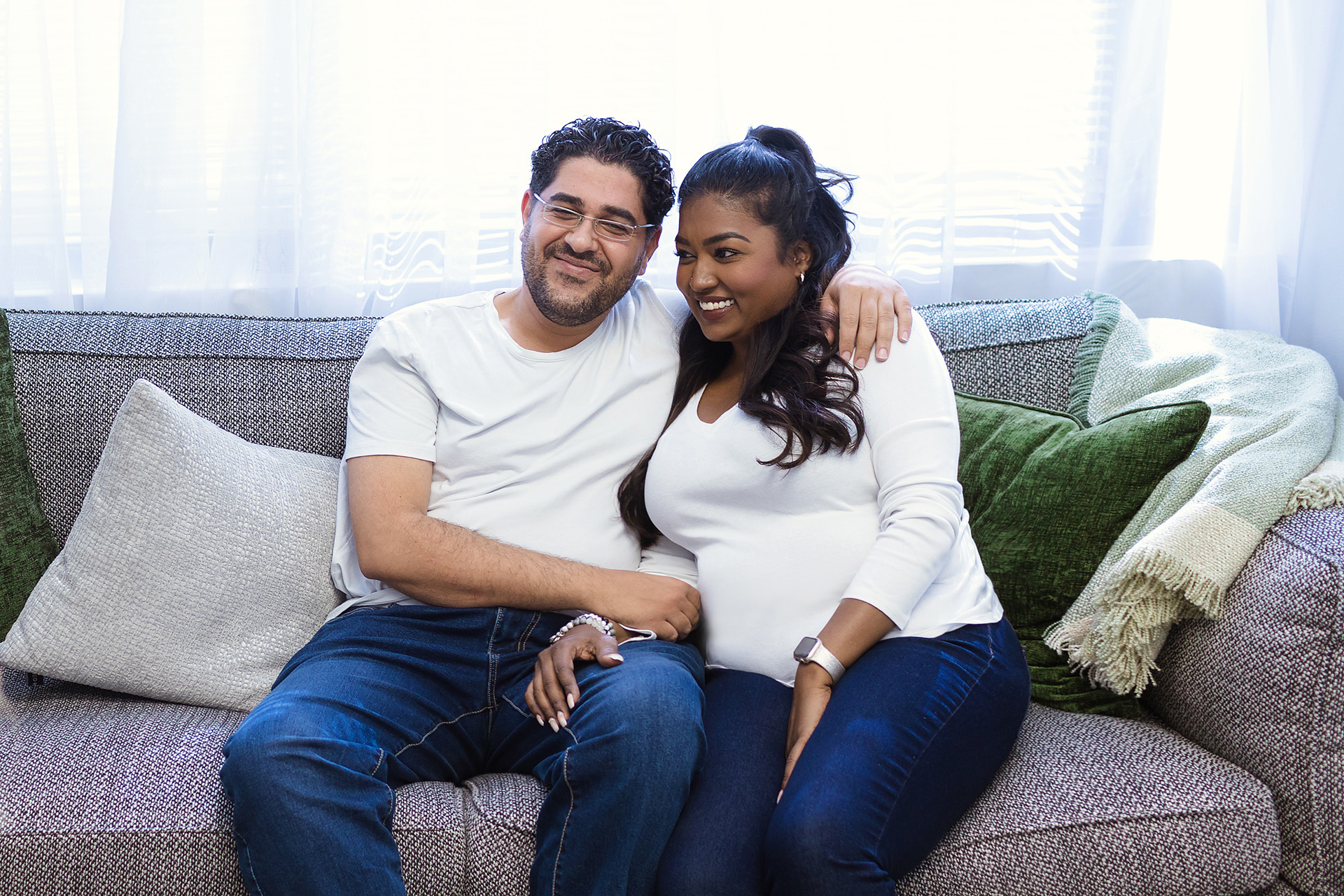 A smiling couple sitting side by side hold hands in a couples therapy session at Couples Reconnect.