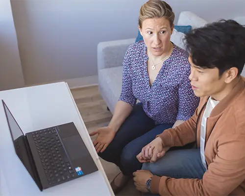 A woman and a man sitting side by side in front of a laptop in an online couples counselling session.